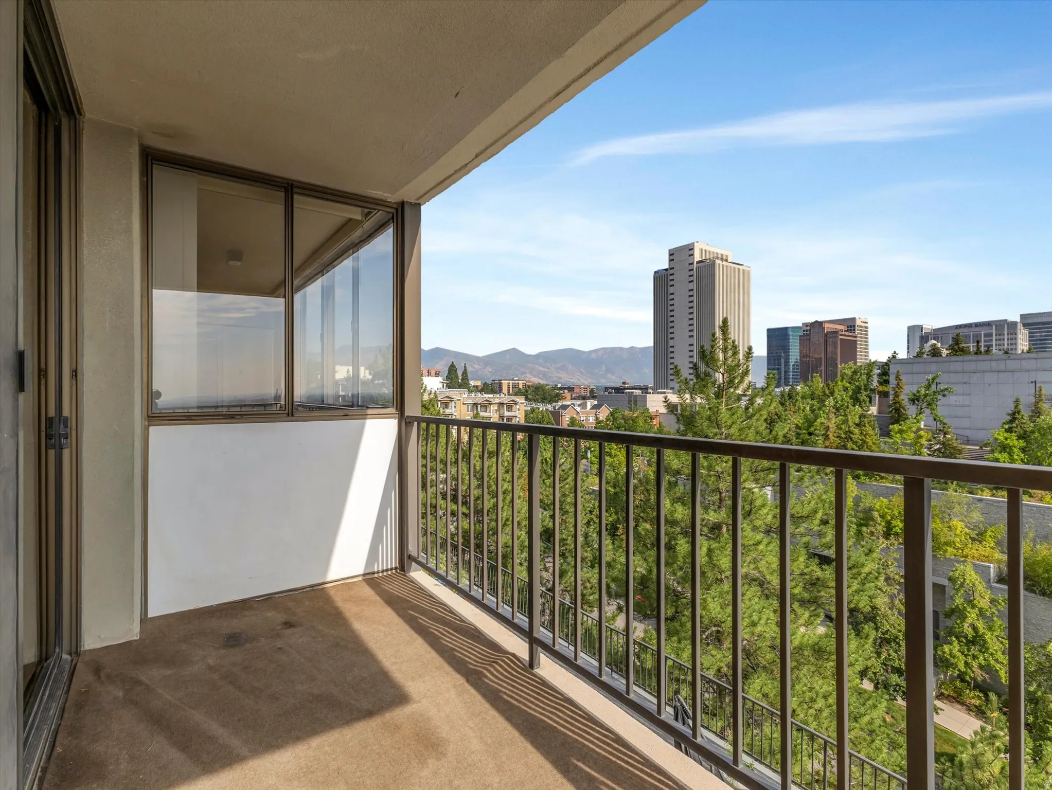 Private balcony with a metal railing, concrete flooring, and surrounding tree canopy