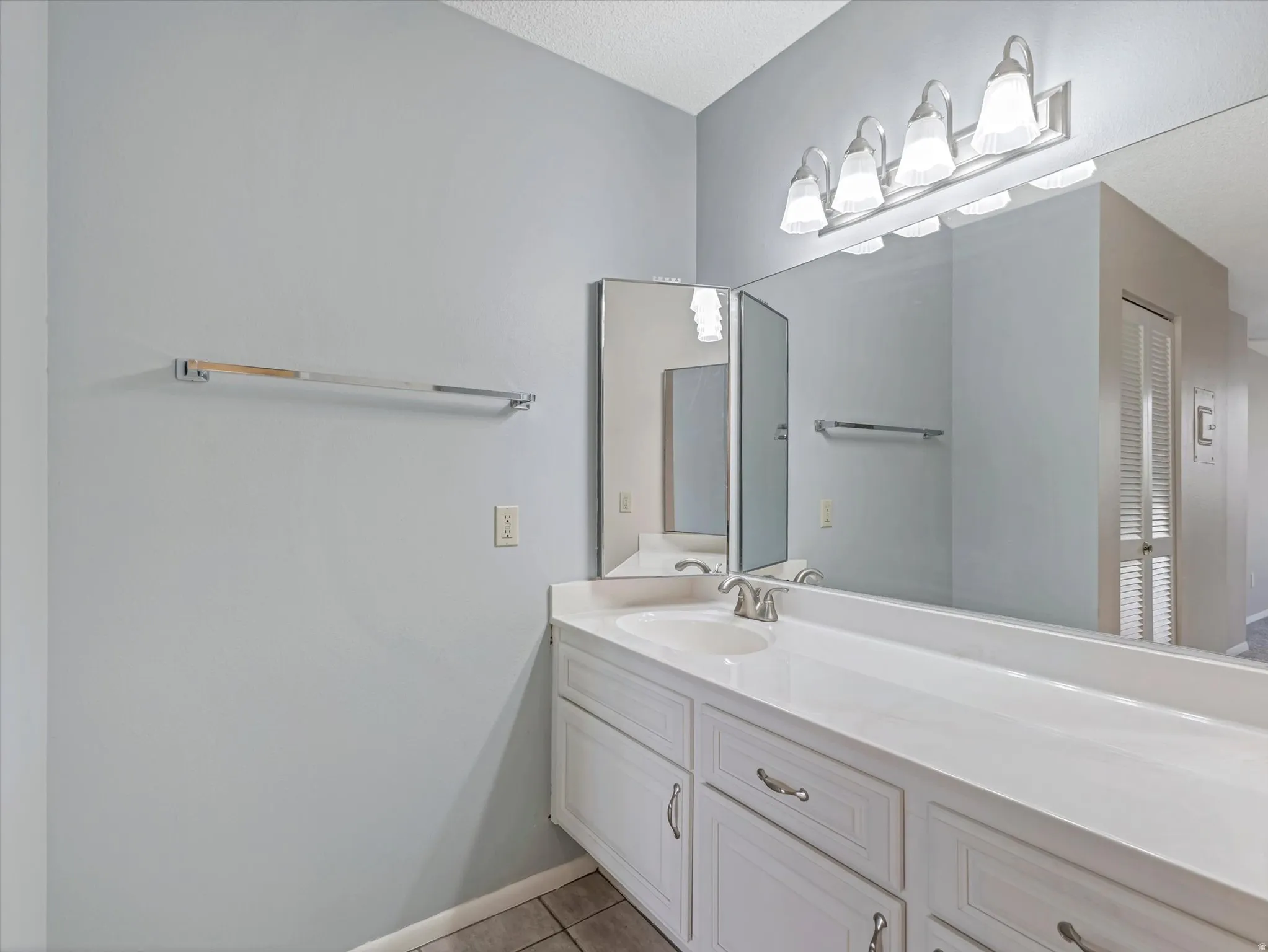 Double vanity with integrated sink, white cabinetry, chrome hardware, and wall-mounted vanity lighting
