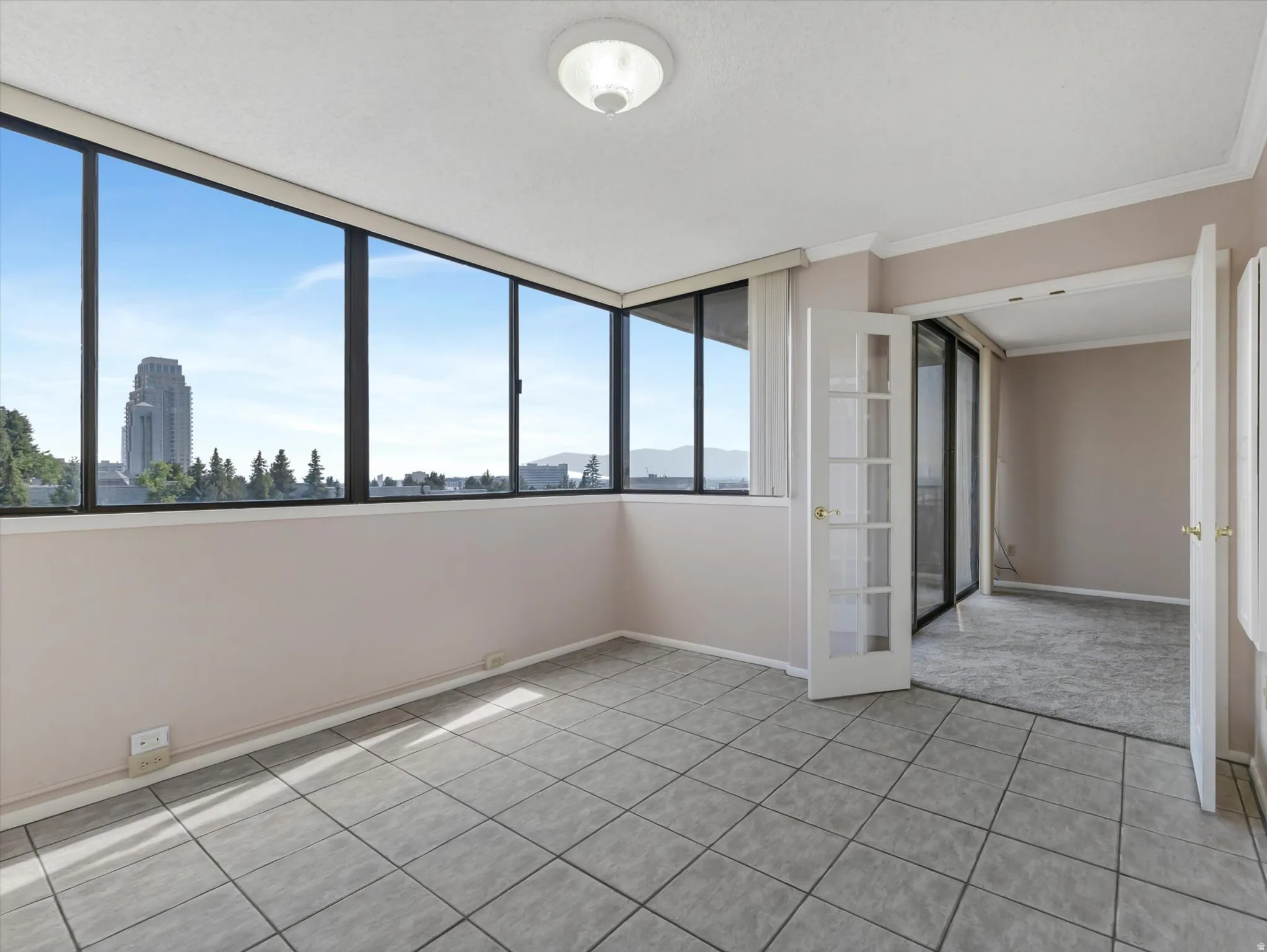 Tile flooring, expansive windows, French doors, crown molding, and a flush mount ceiling light fixture