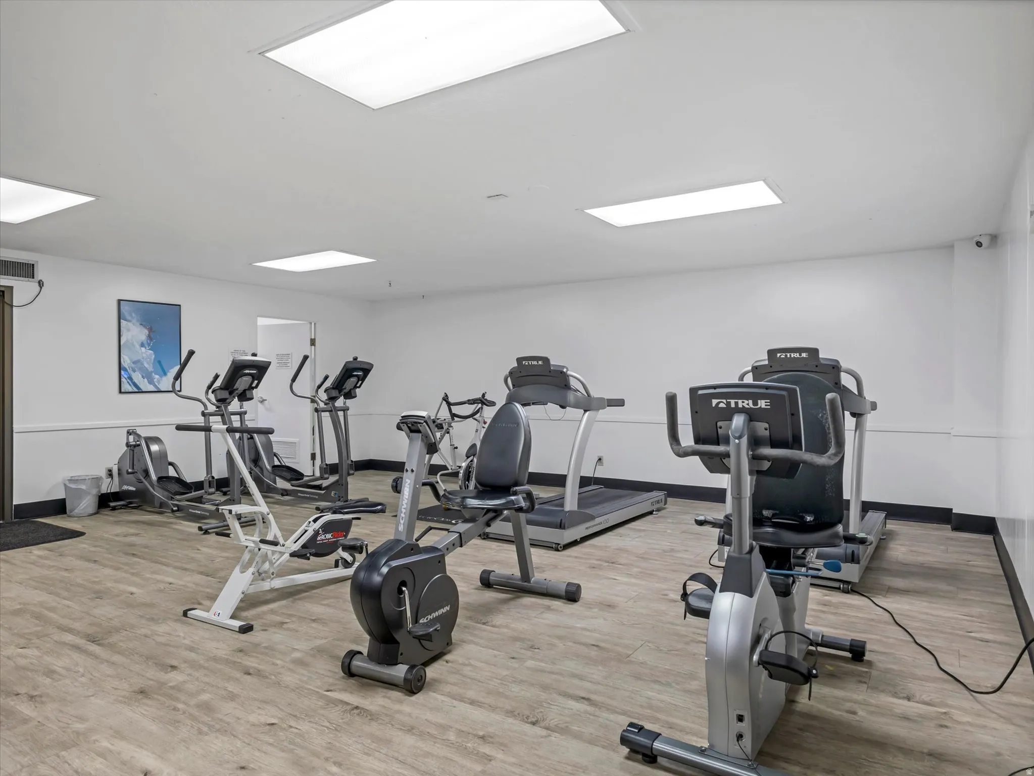 Fitness area with wood-finish flooring, fluorescent lighting, and a selection of exercise equipment