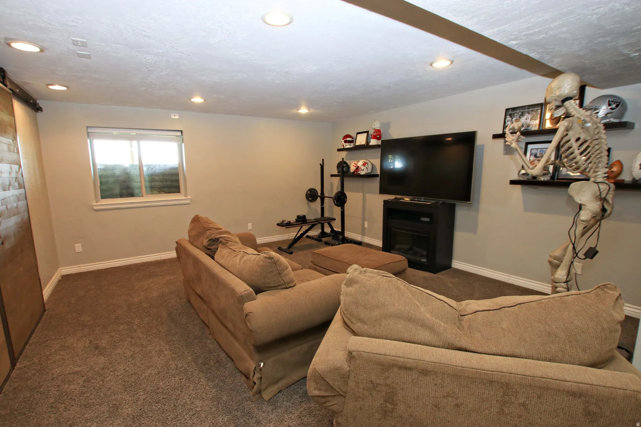 Finished Basement Recreation Room featuring recessed ceiling lighting, carpet flooring, built-in wall shelving, a wall-mounted flat-screen television with media console, and a natural light window