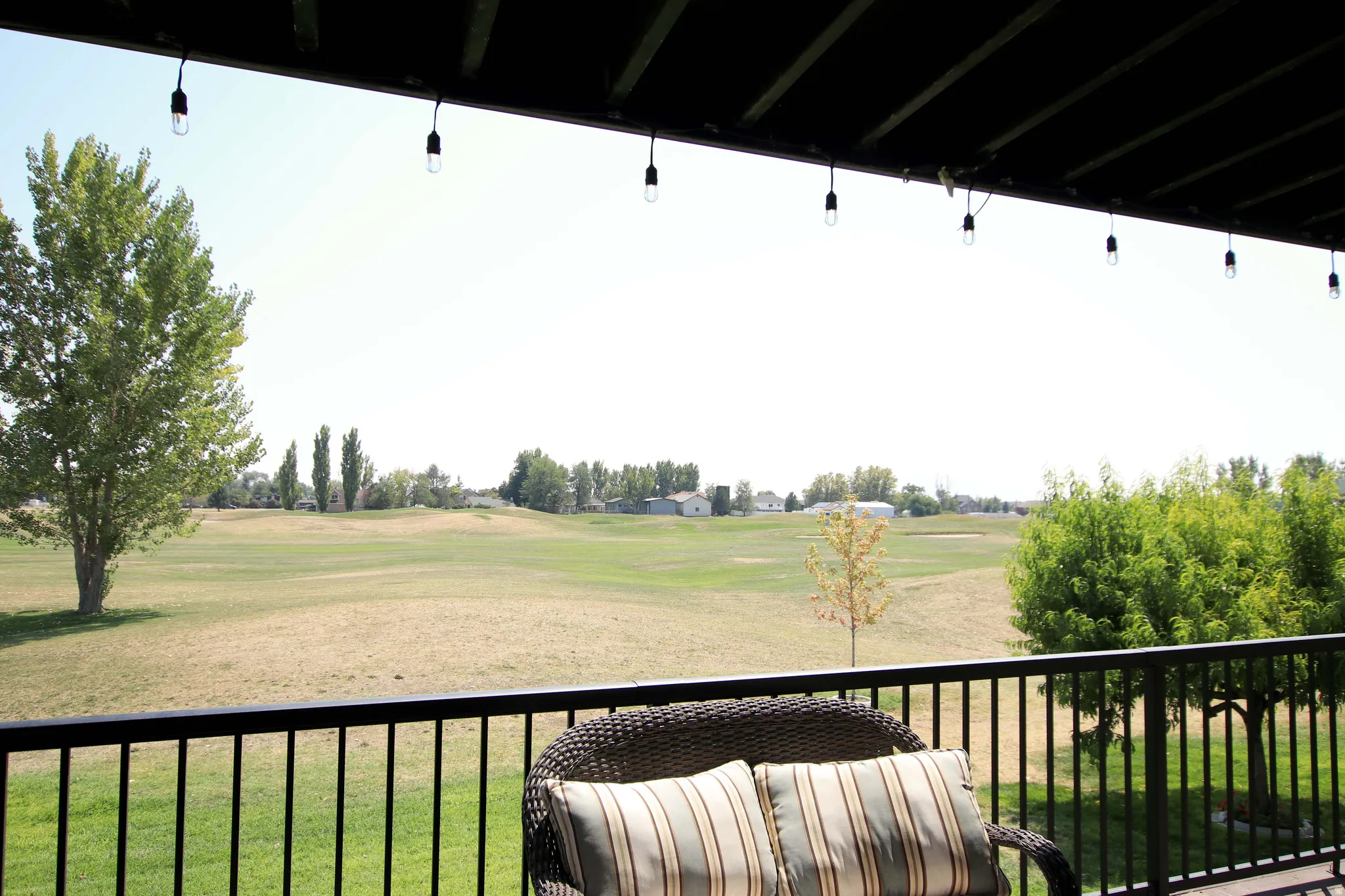 Expansive covered patio with pendant lighting and black metal railings overlooking manicured grounds