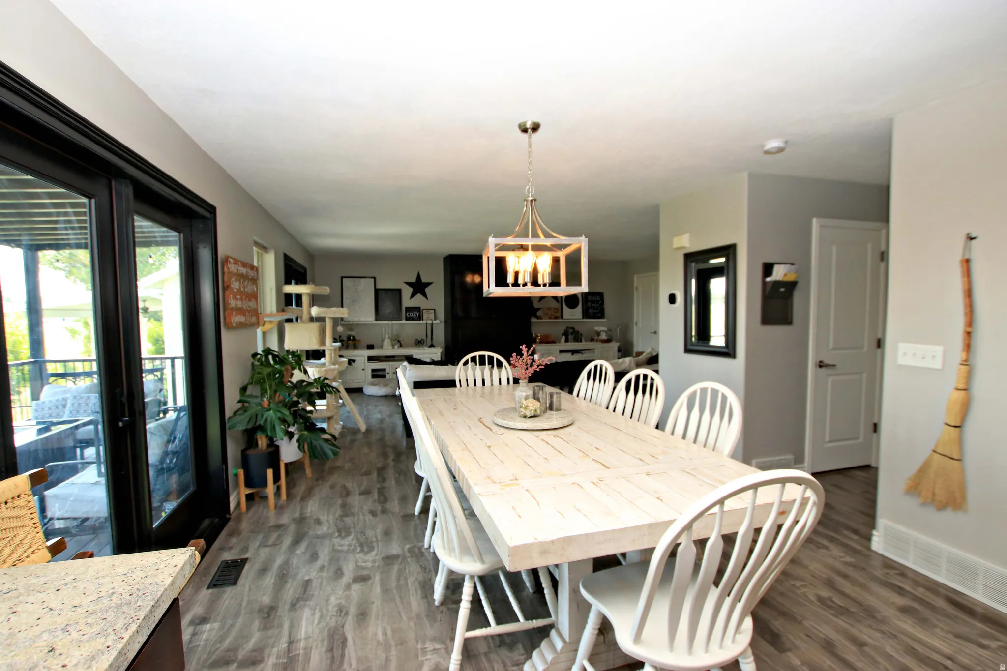 Open-concept dining and kitchen area featuring a light wood-finish dining table with seating for six, pendant lighting with brass fixtures, wood-finish flooring throughout, granite countertops, stainless steel appliances, and sliding glass doors providing