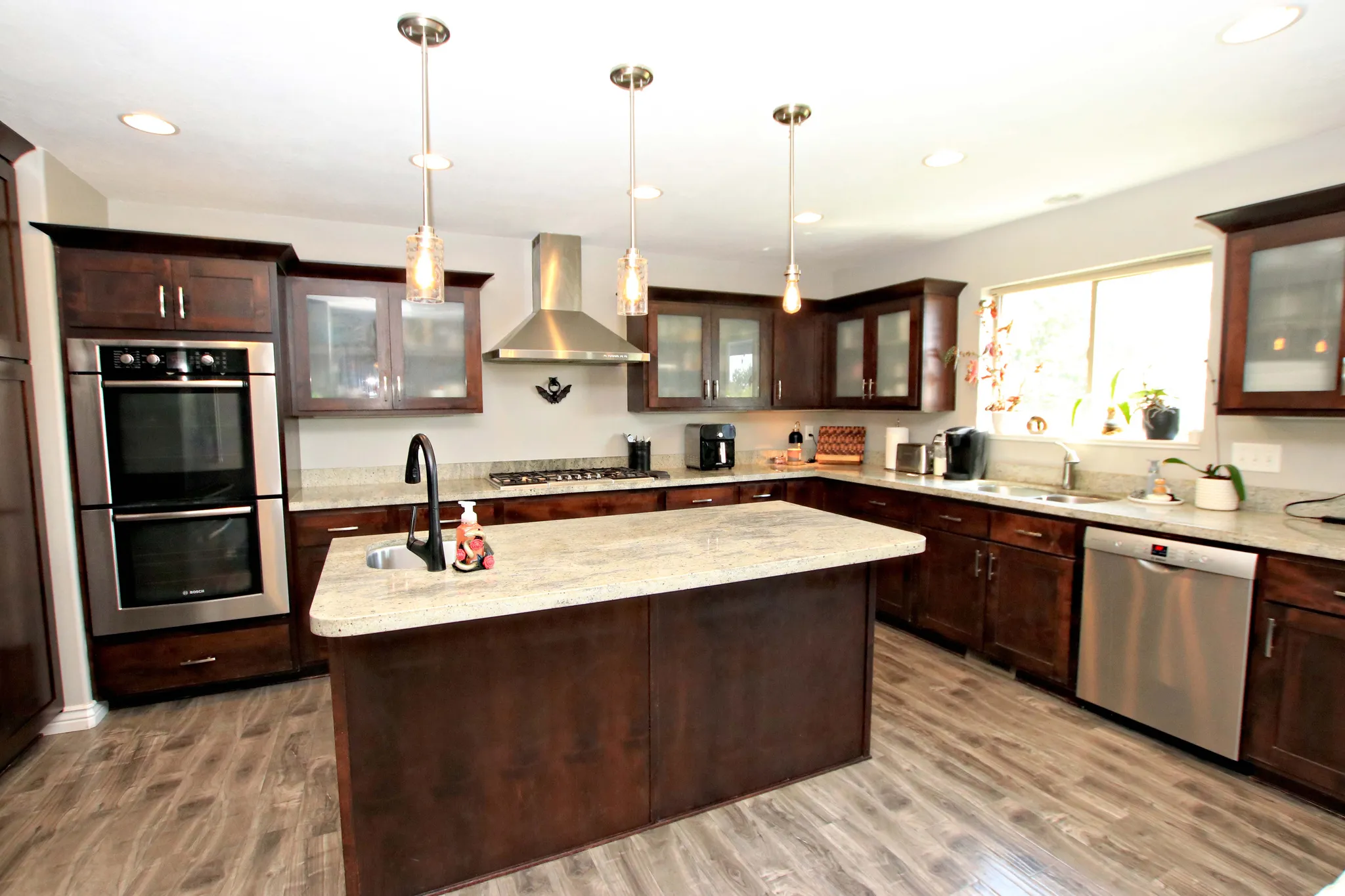 Kitchen featuring an expansive island, wood-finish flooring, dark wood cabinetry, granite countertops, and stainless steel appliances