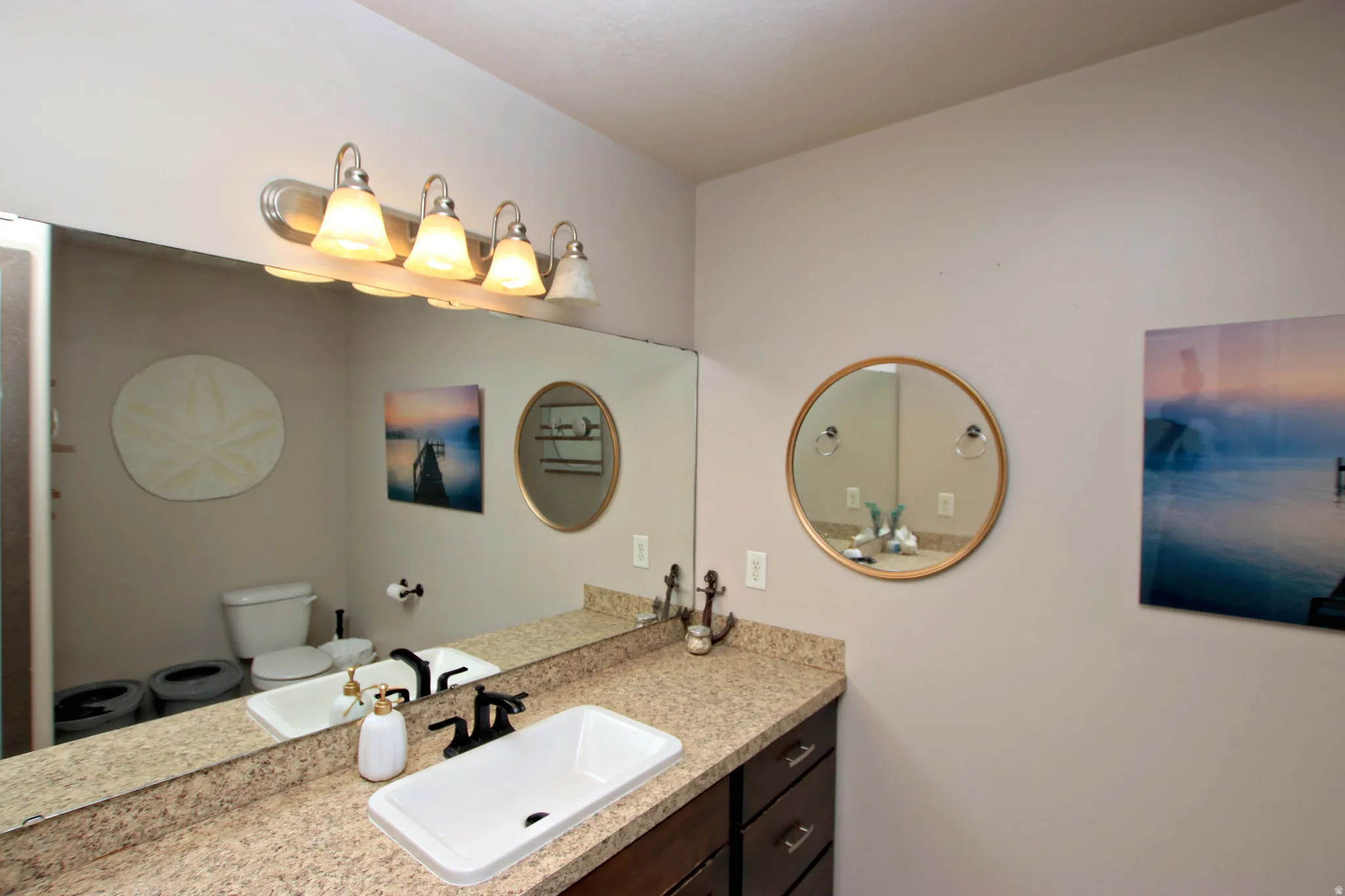 Spa-inspired bathroom featuring a granite-topped vanity with an undermount sink, oil-rubbed bronze fixtures, and abundant natural lighting from a four-light vanity fixture