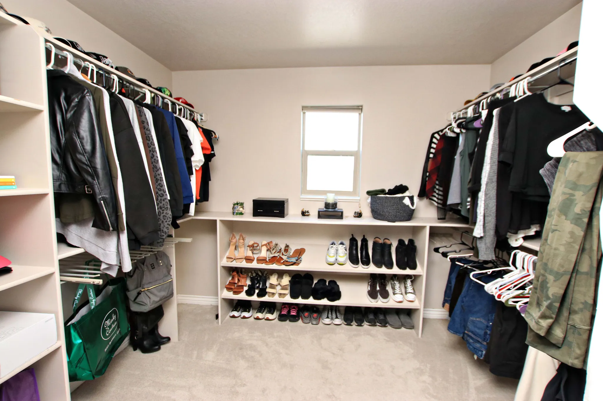Spacious walk-in closet featuring dual clothing rods with ample hanging capacity, built-in shelving with cubbies for organized shoe and accessory storage, natural light from a centered window, and neutral finishes throughout