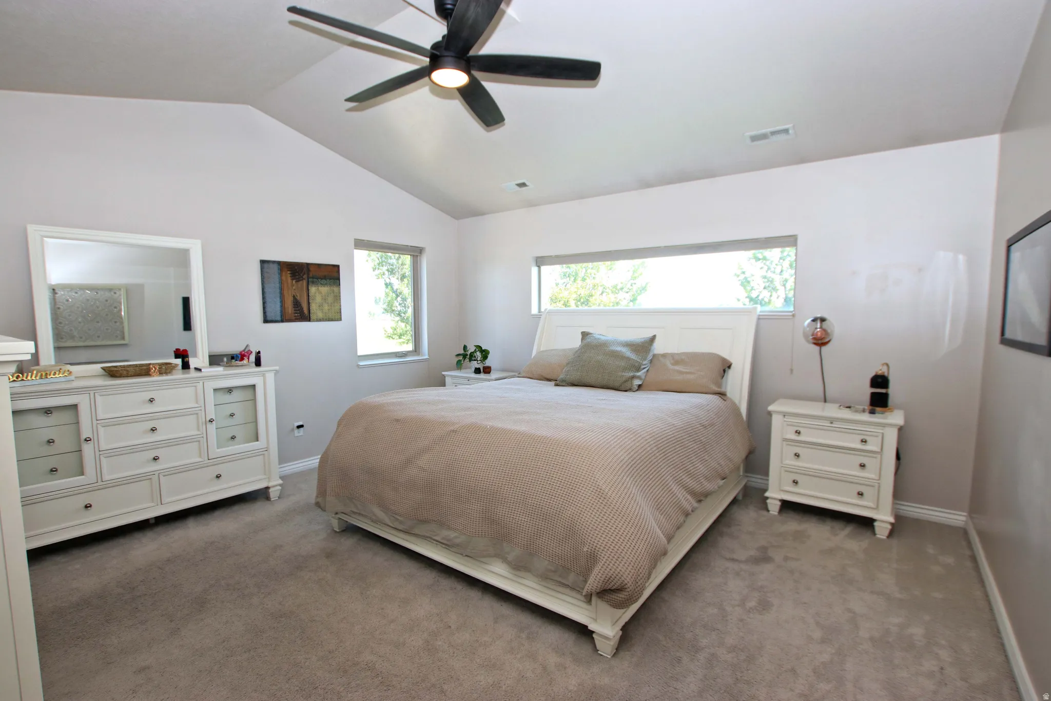Spacious primary bedroom featuring a ceiling fan with integrated lighting, large windows providing natural light, and plush carpeting throughout