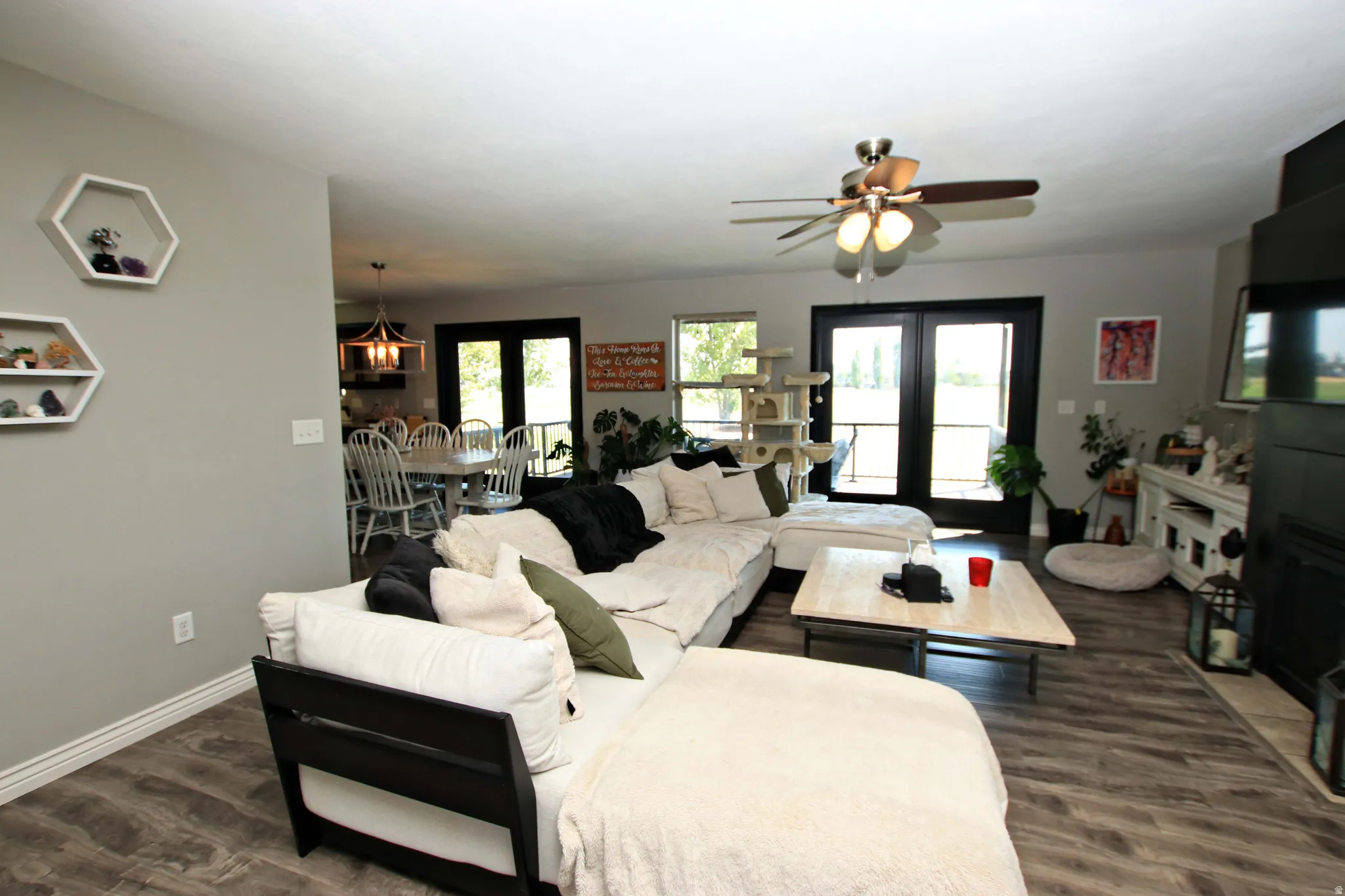 Open-concept living area with wood-finish flooring, a ceiling fan with integrated lighting, and a fireplace with a mantel