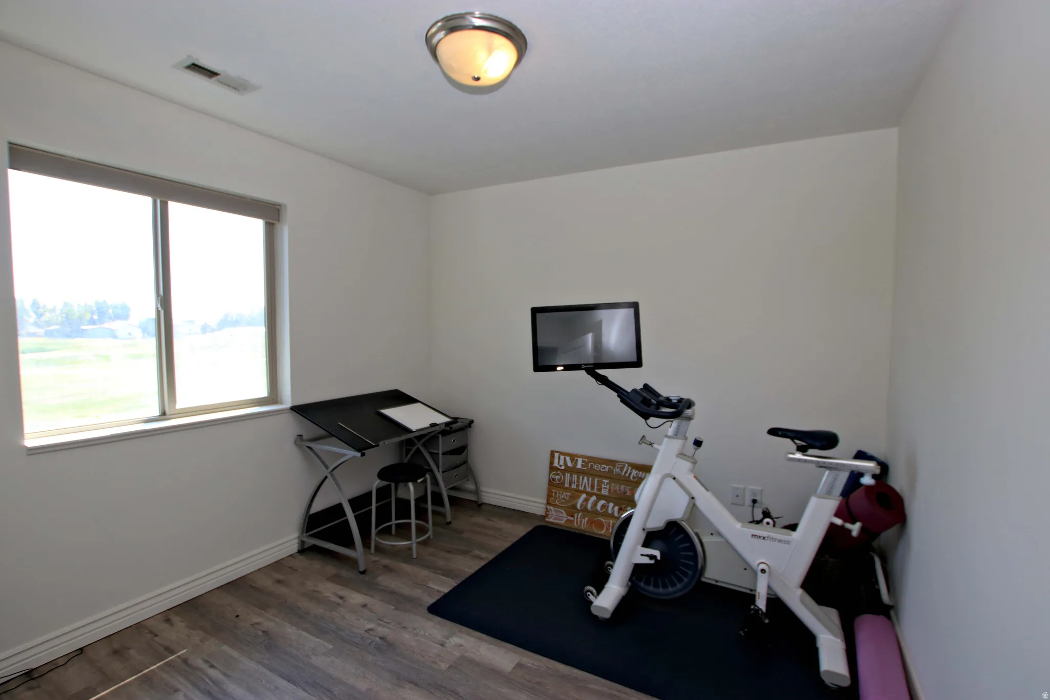 Versatile home office and fitness space featuring wood-finish flooring, abundant natural light from large dual-pane windows, and recessed ceiling lighting