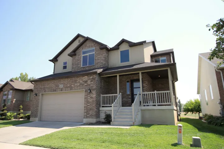 Two-story residence featuring a covered wrap around porch, brick facade, and an attached garage with a paved driveway