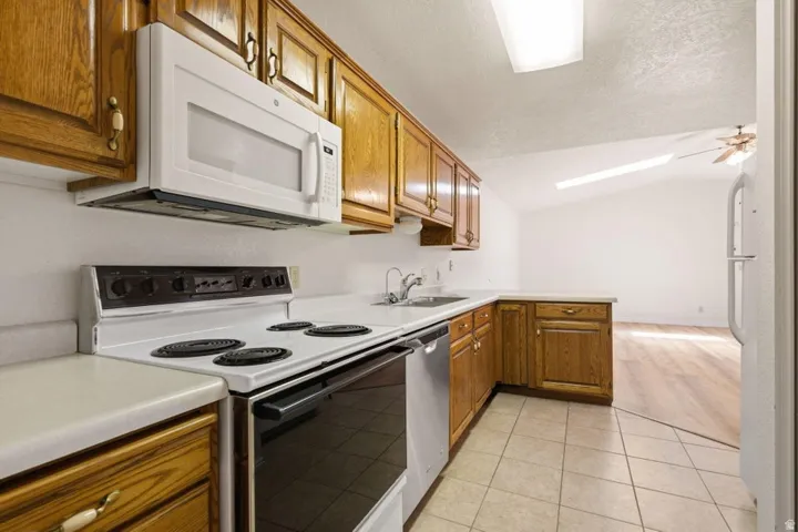 Kitchen featuring wood cabinetry, white appliances, a stainless steel sink, and tile flooring