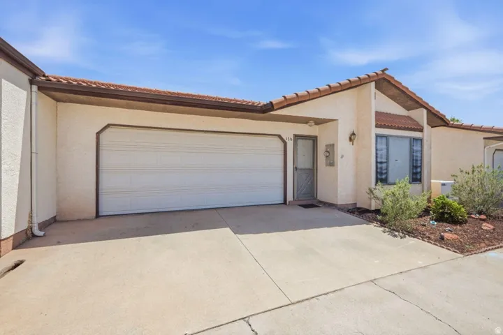 Stucco exterior with a tile roof, an integrated garage, a paved driveway, and a covered entry