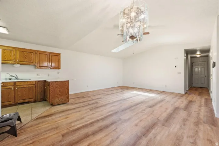 Vaulted ceiling, decorative ceiling fan with lighting, wood-finish flooring, white walls, and wood cabinetry