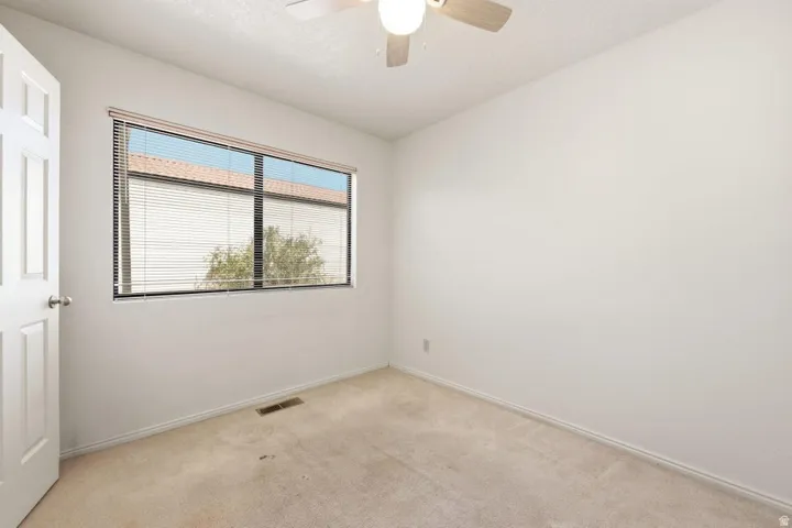 White paneled door, large window with blinds, ceiling fan with integrated lighting, and carpeted flooring