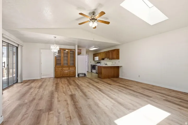 Vaulted ceiling with a skylight and ceiling fan, wood-finish flooring, sliding glass doors, and a built-in wood hutch