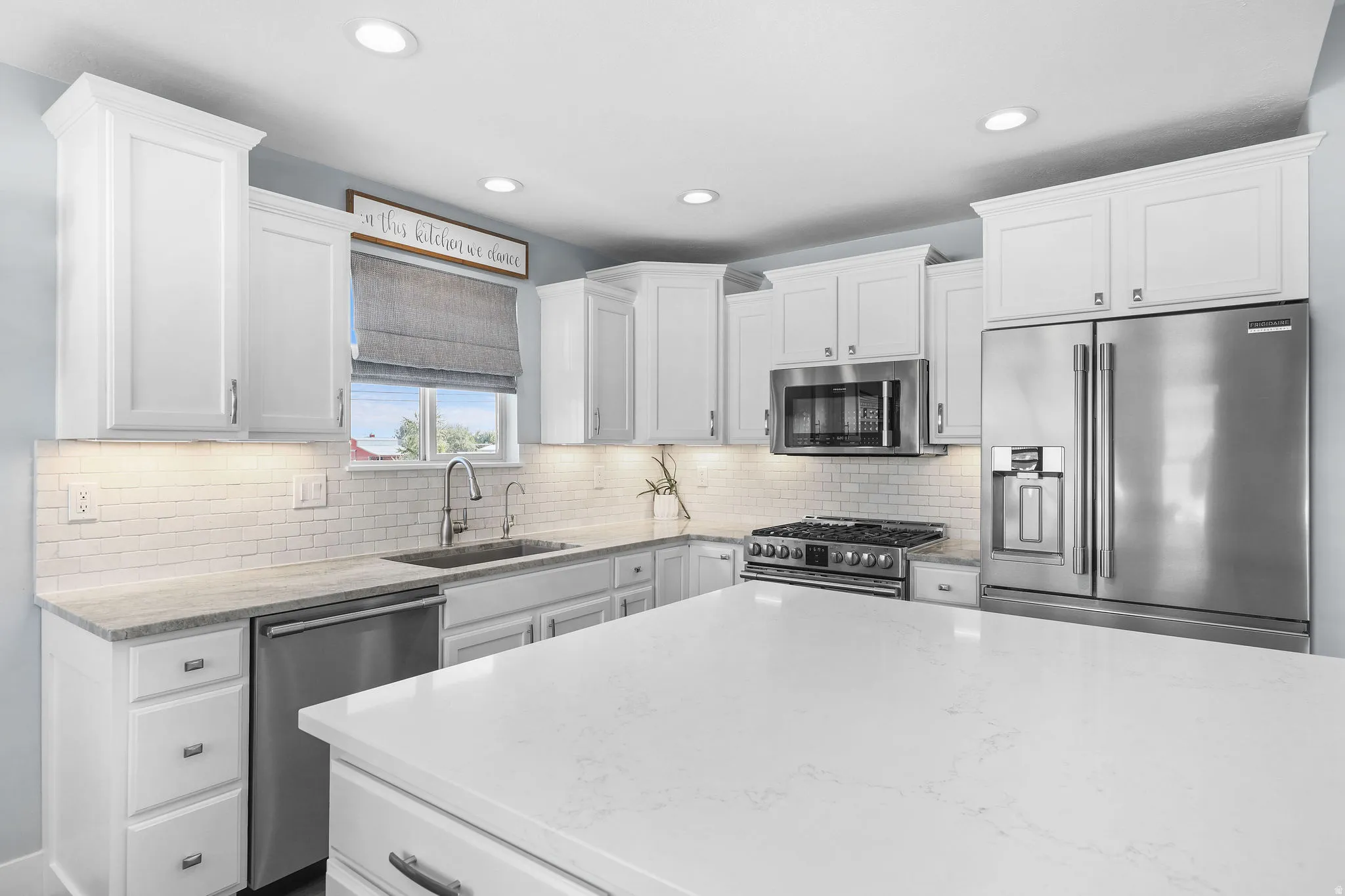 White shaker cabinetry, stainless steel appliances, subway tile backsplash, recessed lighting, and a large central island with a solid surface countertop