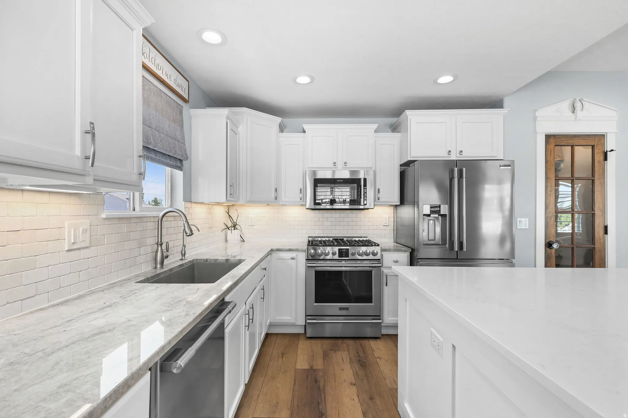 Kitchen featuring white shaker cabinetry, stainless steel appliances, wood-finish flooring, white subway tile backsplash, and light-toned countertops