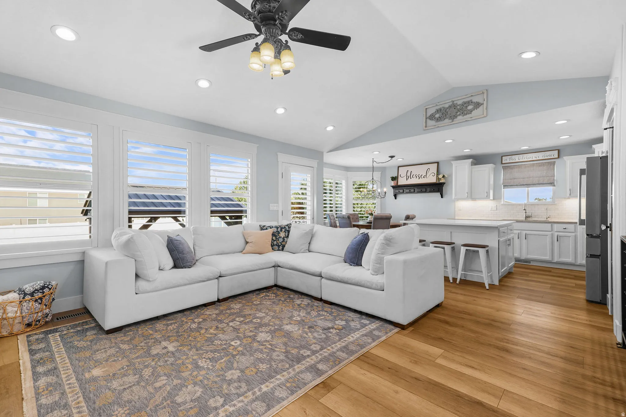 Vaulted ceiling with recessed lighting and ceiling fan, wood-finish flooring, white plantation shutters, and a kitchen featuring white cabinetry and an island