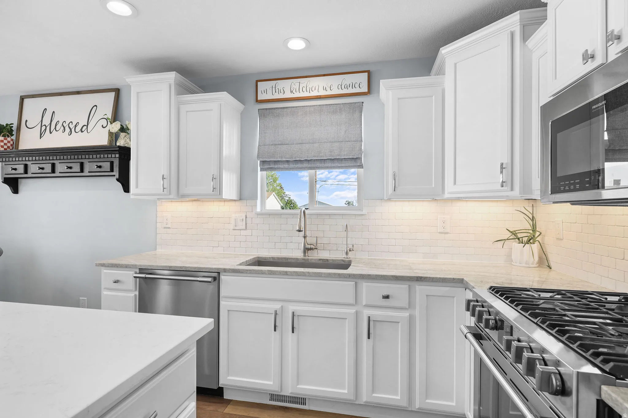 White shaker-style cabinetry with crown molding, light-toned countertops, subway tile backsplash, stainless steel dishwasher, and stainless steel gas range