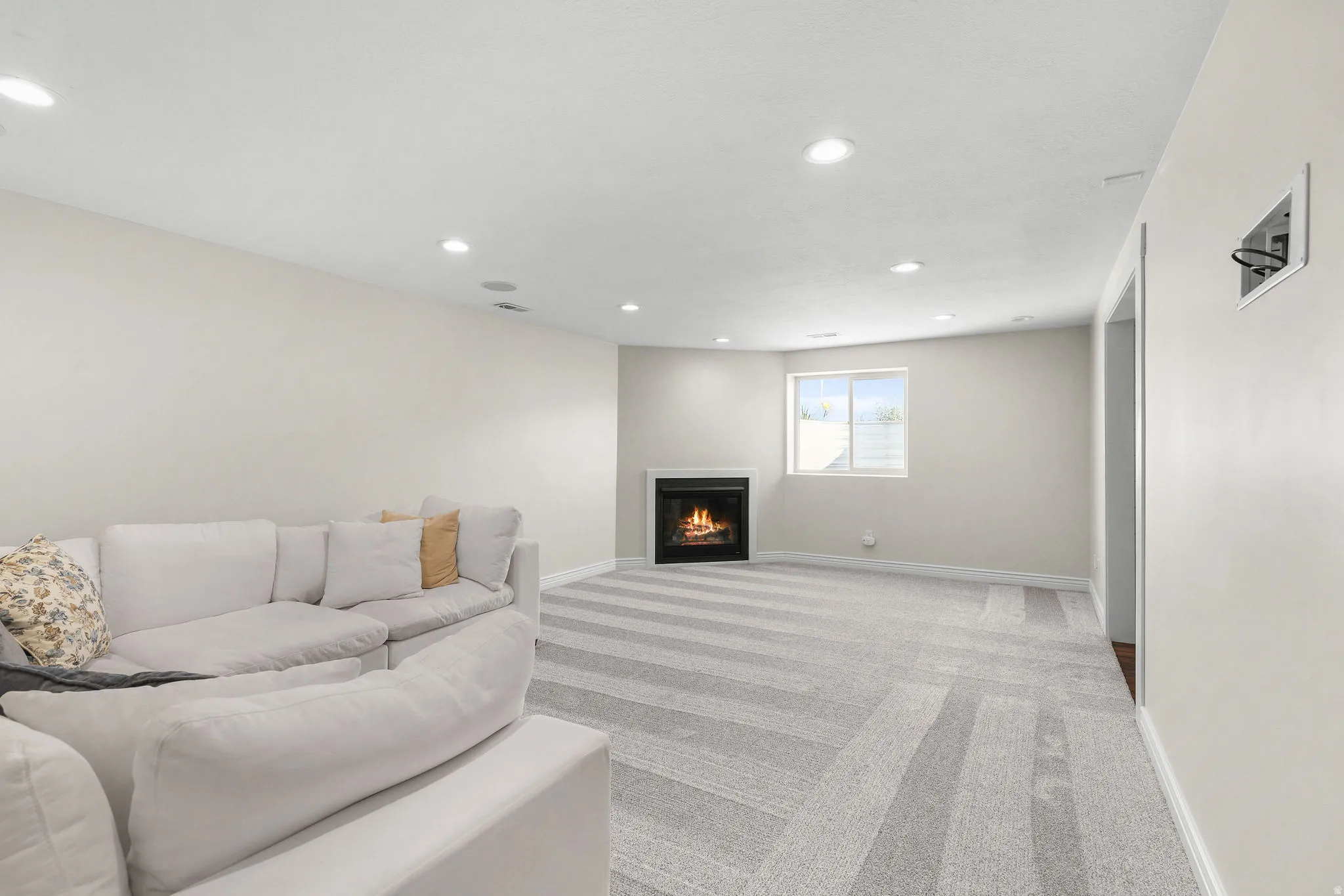 Recessed lighting illuminates the space, featuring a fireplace, light-toned walls, a window, and patterned carpeting