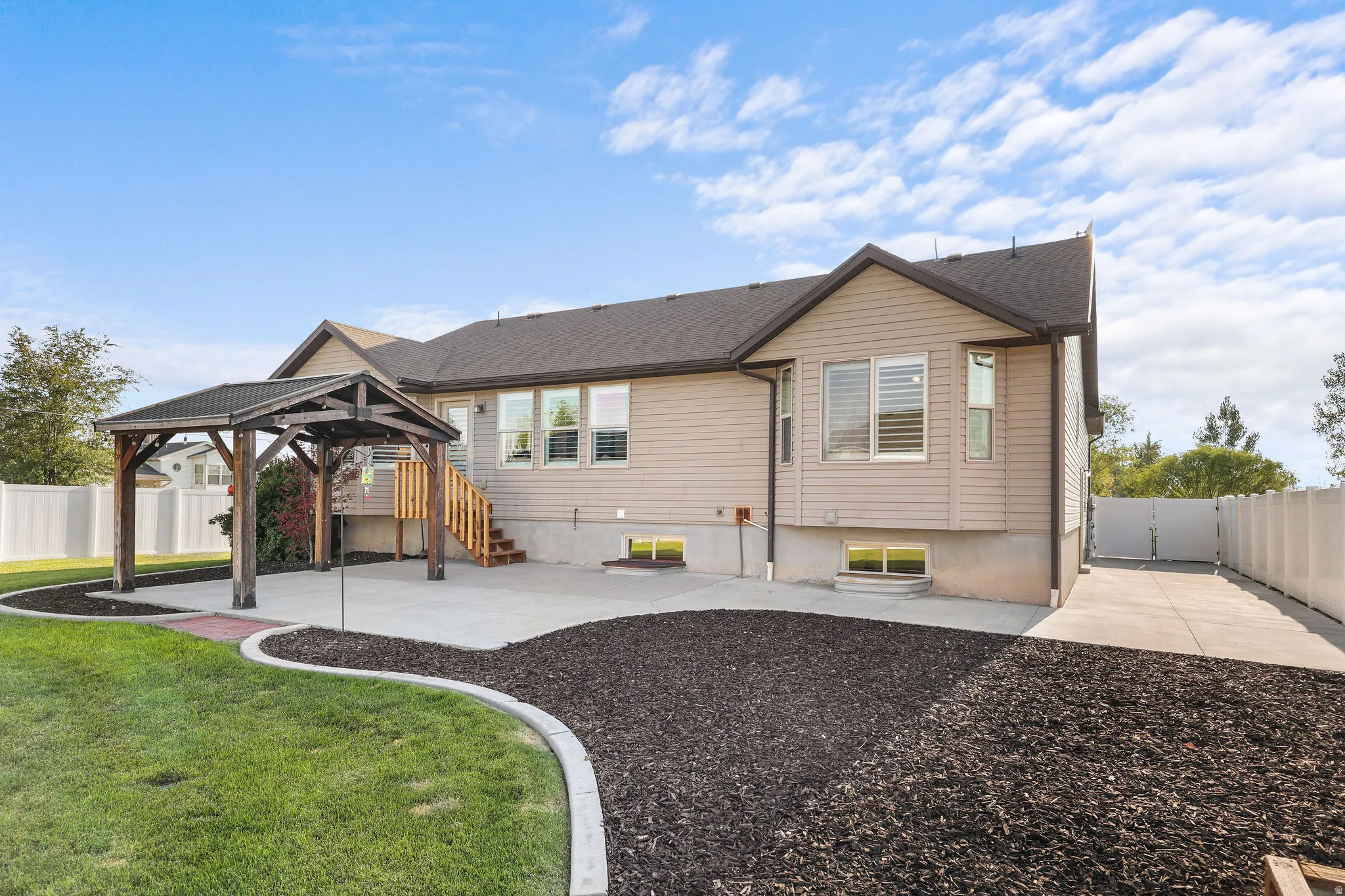 Expansive backyard featuring a concrete patio, wooden pergola, and a manicured lawn