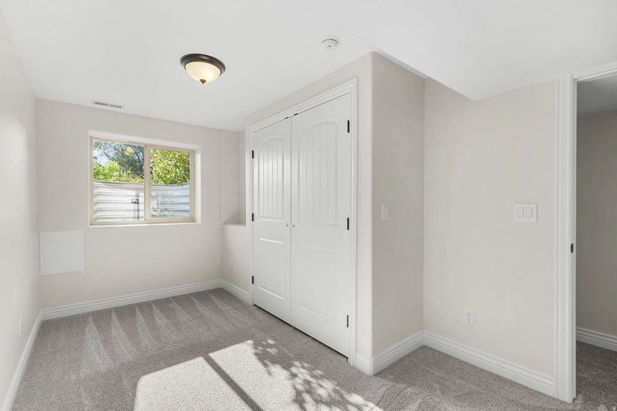 Neutral wall paint, gray carpet flooring, window with white trim, white paneled closet doors, and a ceiling-mounted light fixture