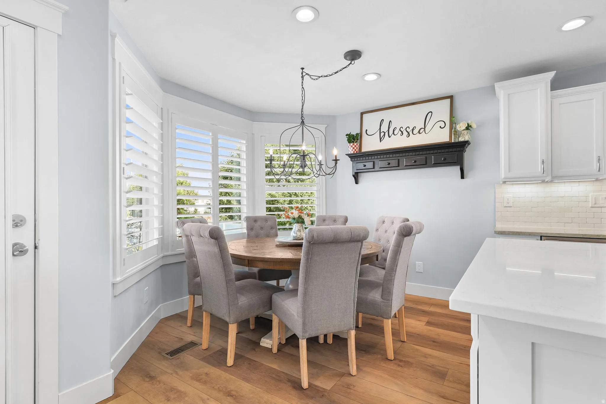 Bay window with plantation shutters, wood-finish flooring, recessed lighting, white cabinetry, and subway tile backsplash
