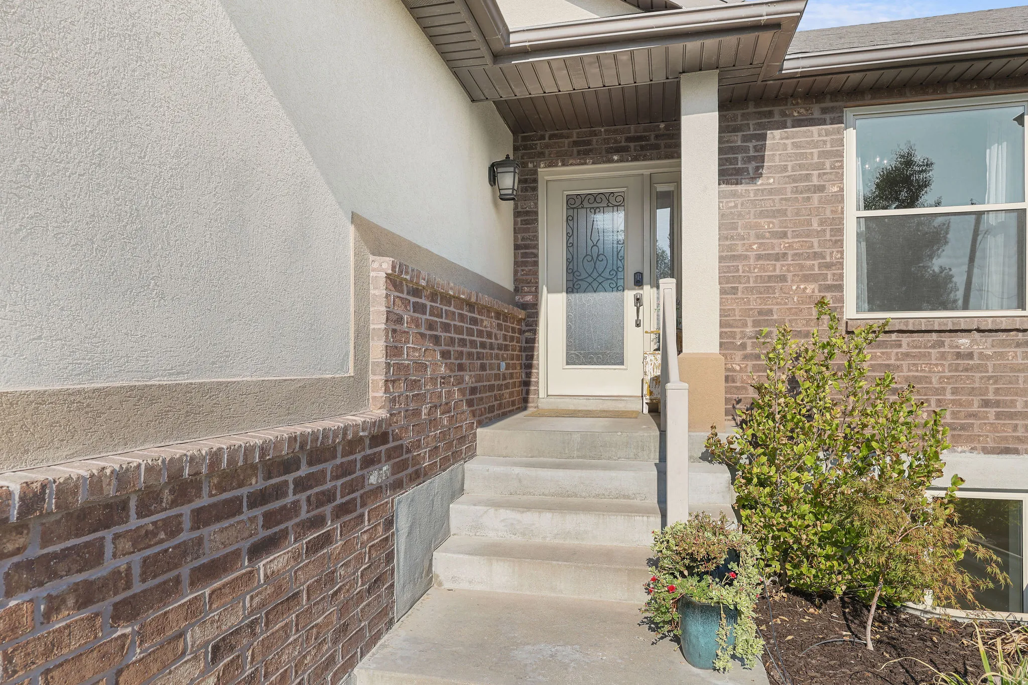Brick and stucco exterior with concrete steps leading to an entry door featuring decorative glass