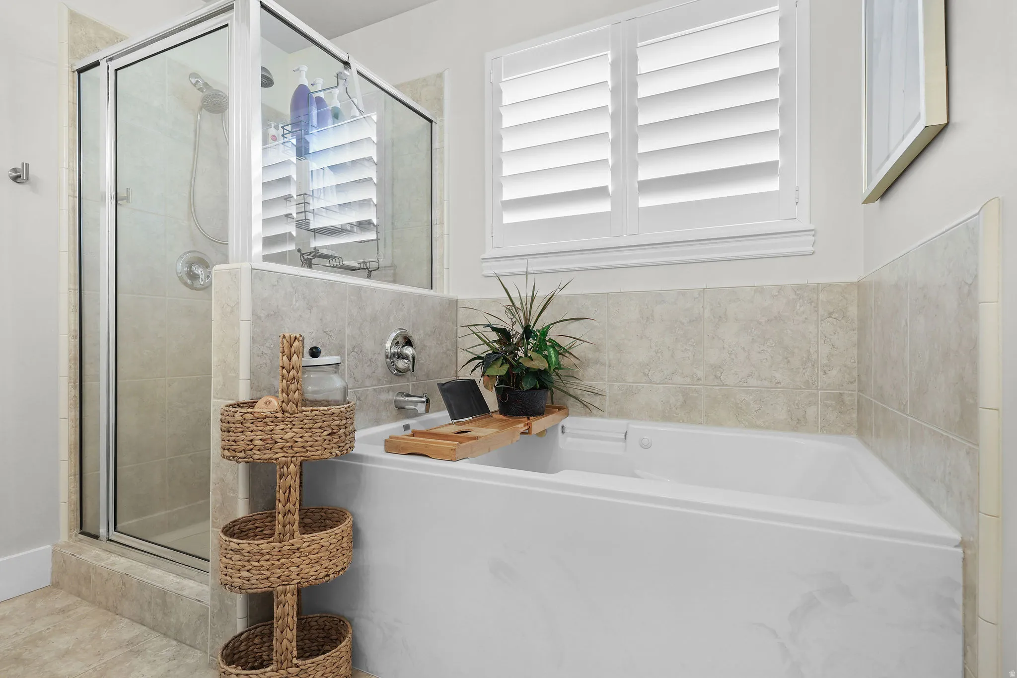 Built-in soaking tub with surrounding tile, separate glass-enclosed shower, and window with plantation shutters