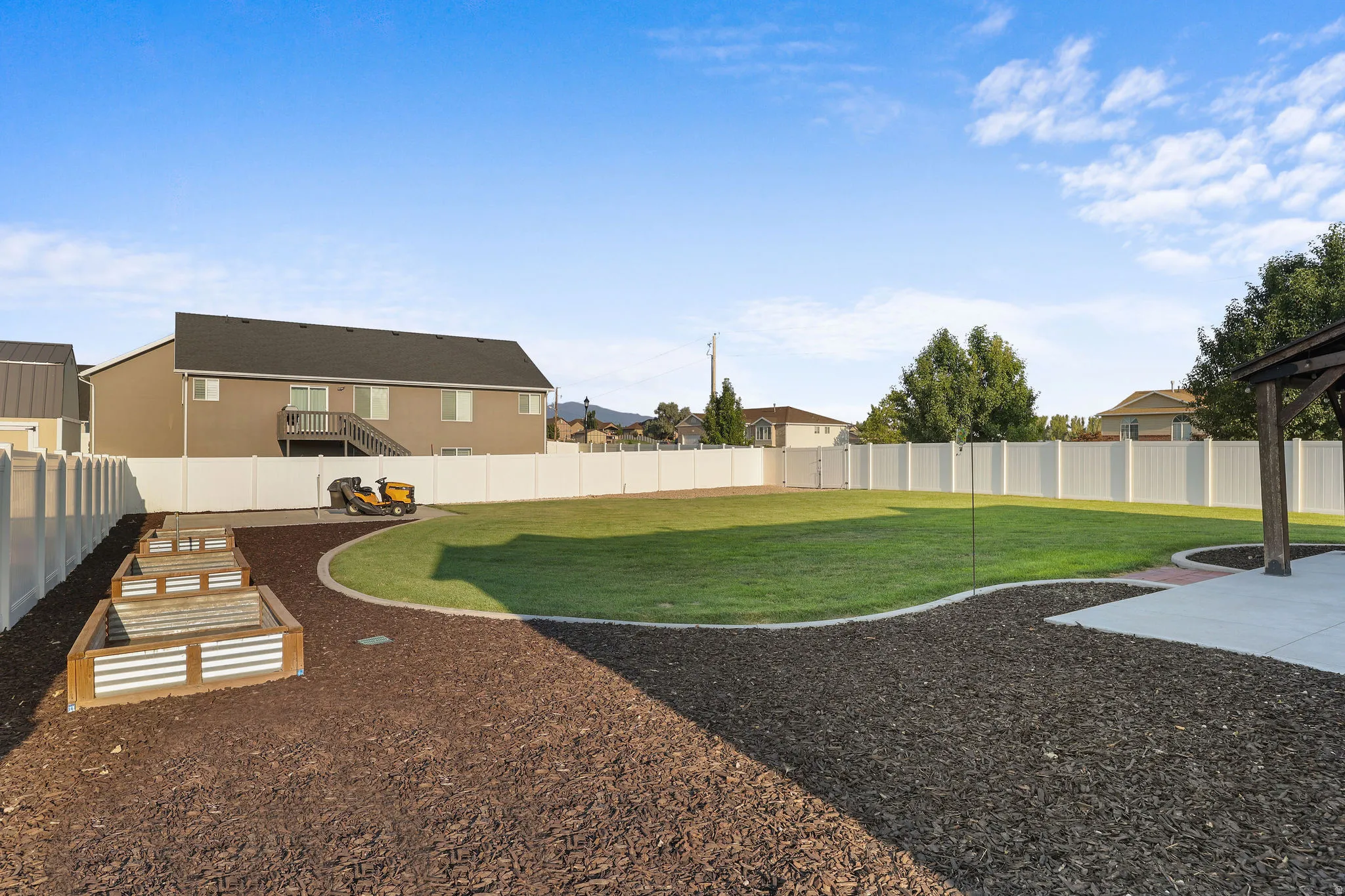 Expansive backyard featuring a manicured lawn, established planter boxes, concrete patio, and full perimeter fencing