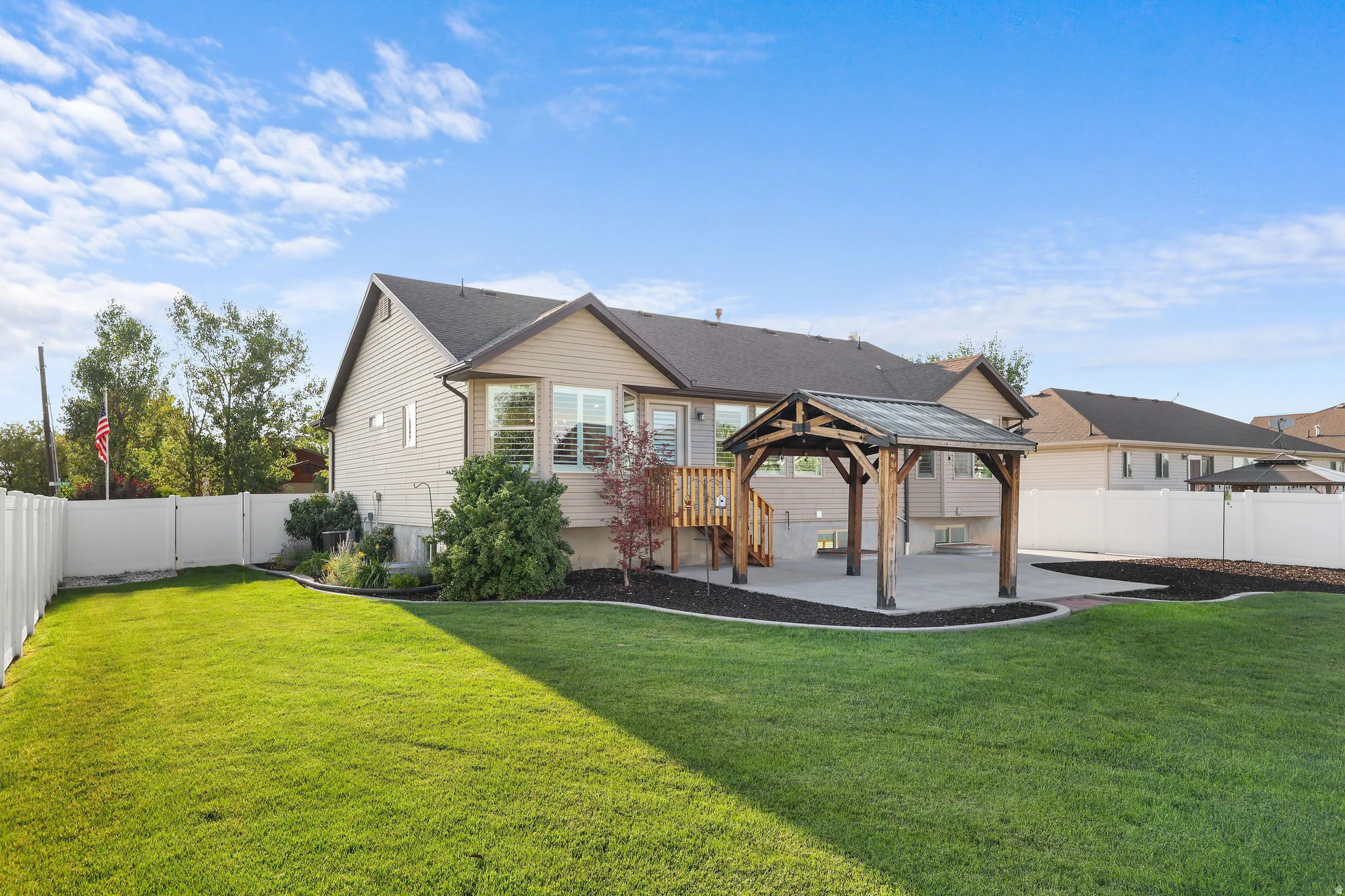Expansive backyard featuring a manicured lawn, a concrete patio, a wooden pergola, a privacy fence, and mature landscaping