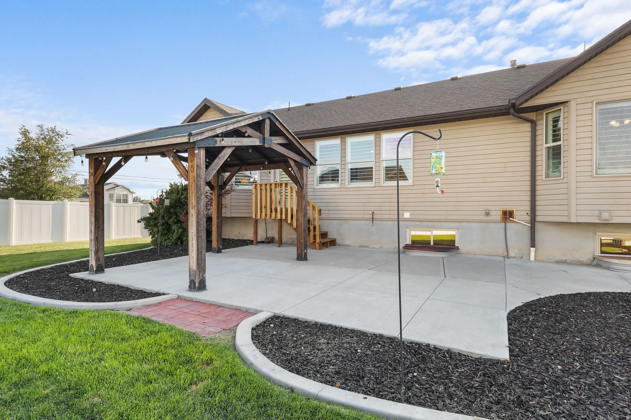 Concrete patio featuring a wood-frame gazebo and surrounding landscape beds