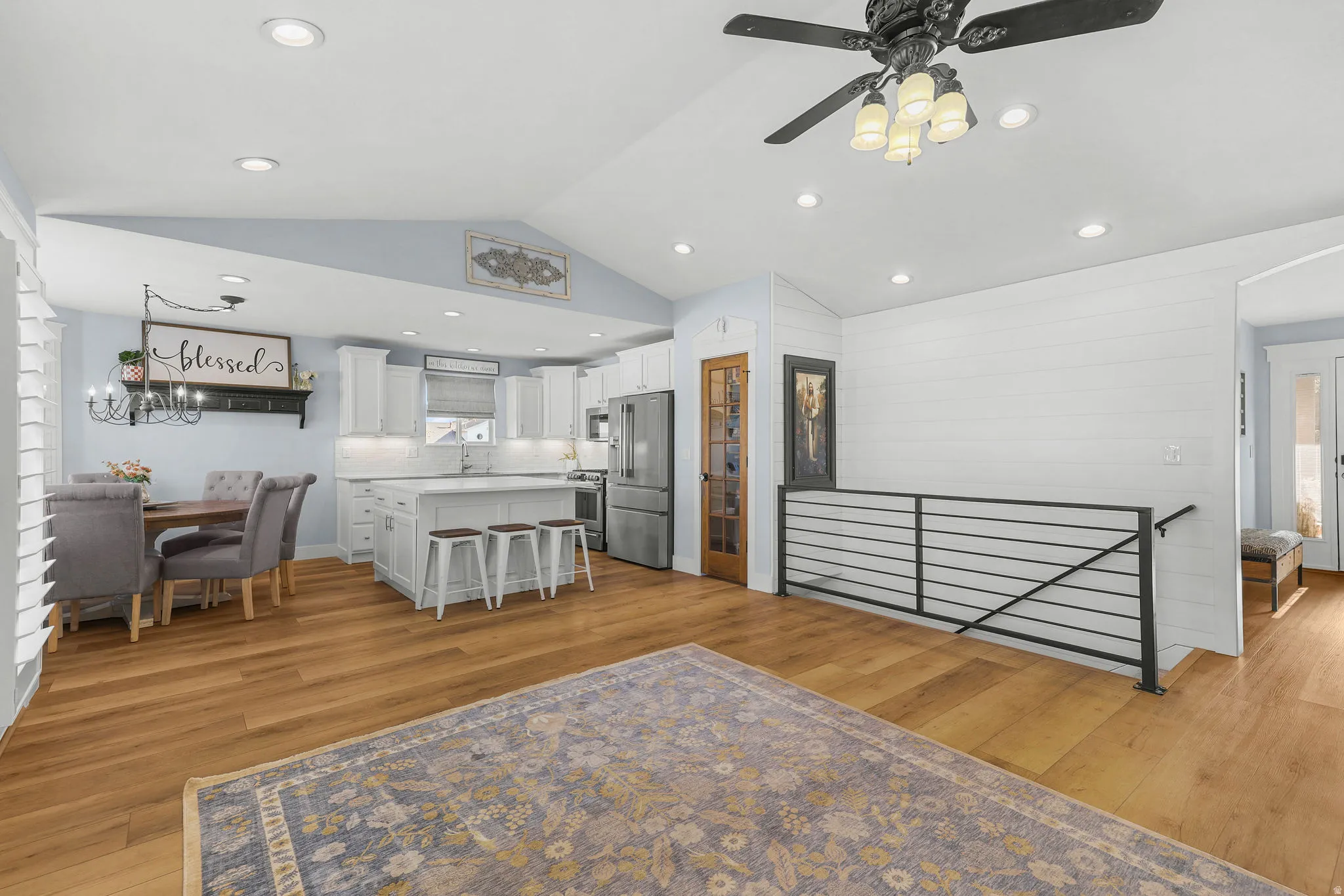 Vaulted ceilings with recessed lighting, wood-finish flooring, white kitchen cabinetry, a kitchen island with seating, and a modern horizontal railing