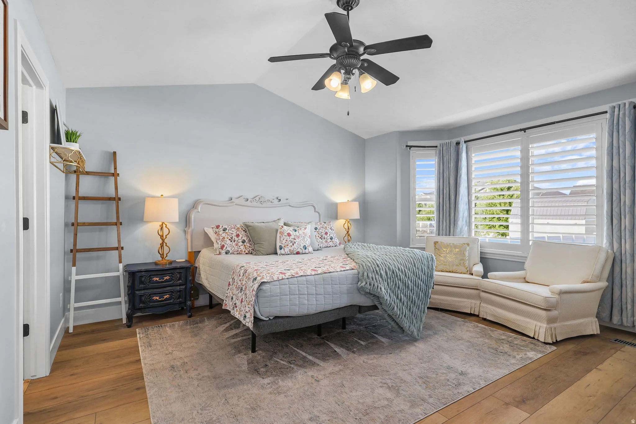 Vaulted ceiling with a ceiling fan, bay window with plantation shutters, wood-finish flooring