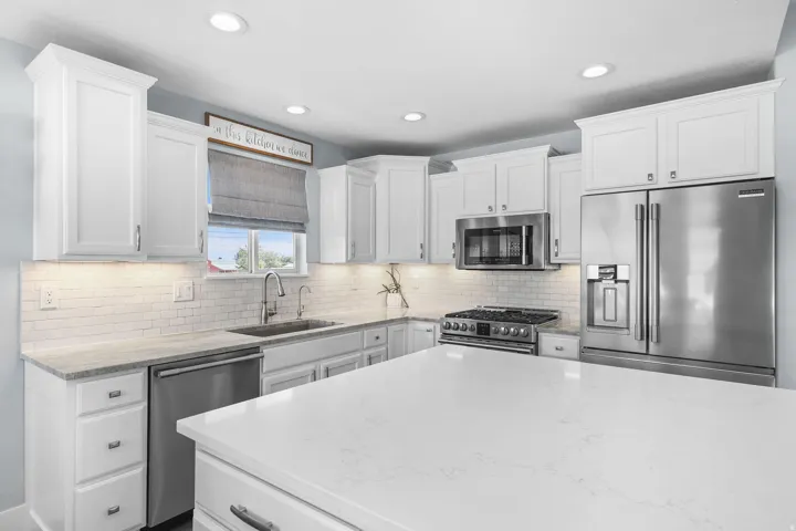 White shaker cabinetry, stainless steel appliances, subway tile backsplash, recessed lighting, and a large central island with a solid surface countertop