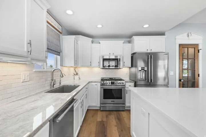 Kitchen featuring white shaker cabinetry, stainless steel appliances, wood-finish flooring, white subway tile backsplash, and light-toned countertops