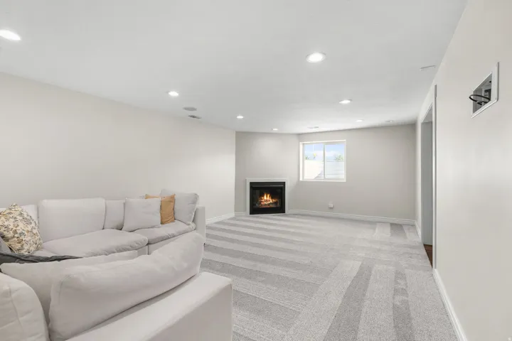 Recessed lighting illuminates the space, featuring a fireplace, light-toned walls, a window, and patterned carpeting