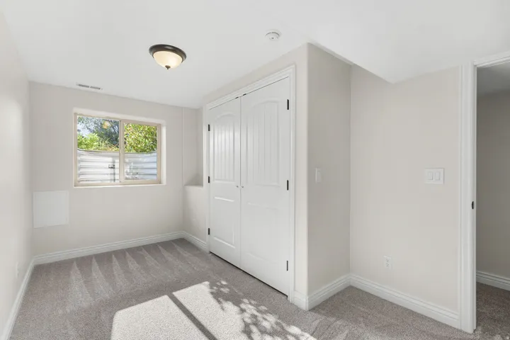 Neutral wall paint, gray carpet flooring, window with white trim, white paneled closet doors, and a ceiling-mounted light fixture