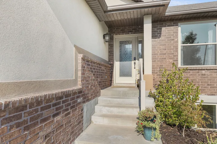 Brick and stucco exterior with concrete steps leading to an entry door featuring decorative glass