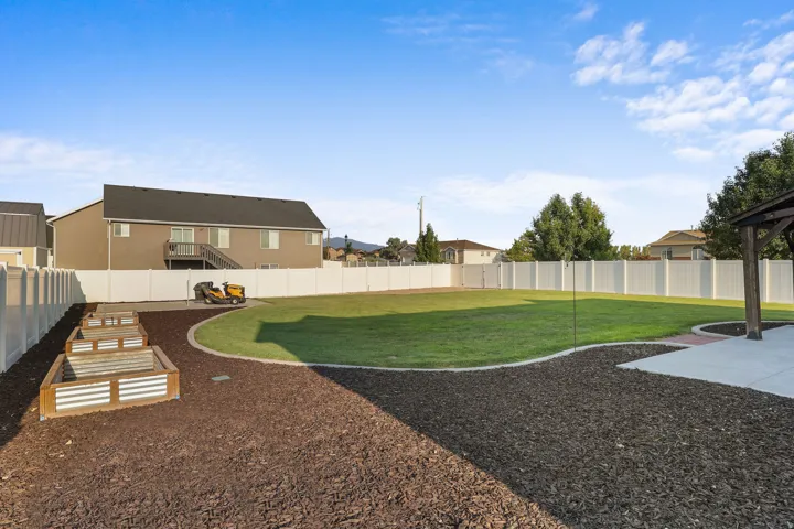 Expansive backyard featuring a manicured lawn, established planter boxes, concrete patio, and full perimeter fencing