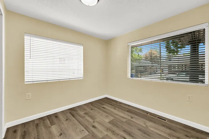 Wood-finish flooring, two windows with horizontal blinds, and neutral wall paint