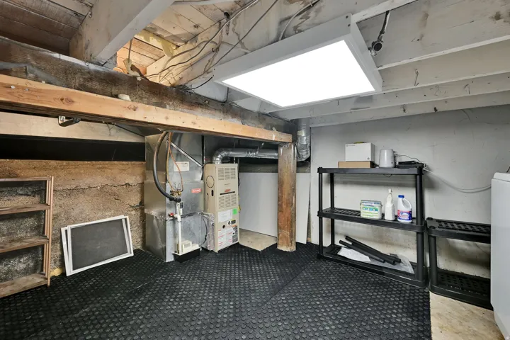 Exposed ceiling joists, concrete foundation wall, forced-air furnace, water heater, and utility lighting