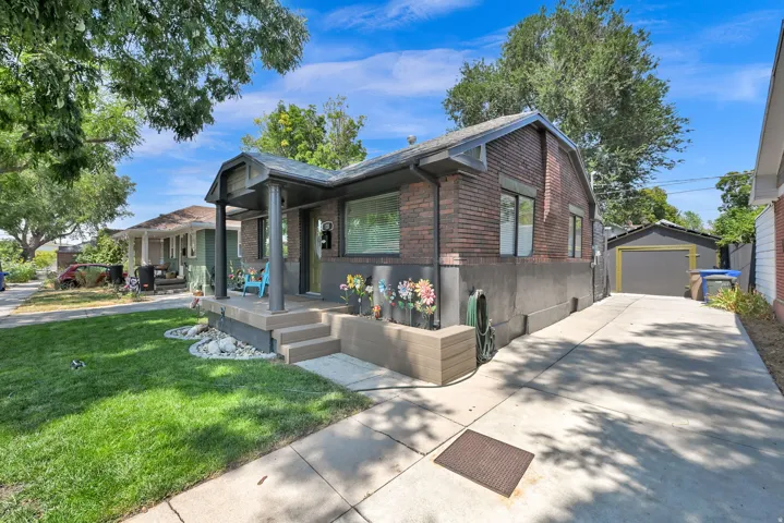 Brick facade residence featuring a covered front porch, concrete driveway, and detached garage