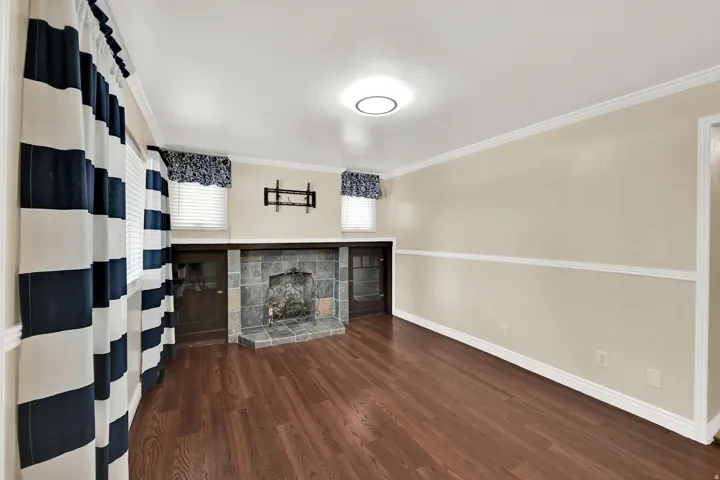 Hardwood-finish flooring, stone-tiled fireplace with hearth, built-in cabinetry, crown molding, and recessed lighting