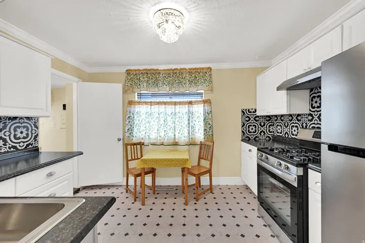 Kitchen featuring white cabinetry, dark countertops, a stainless steel gas range, and a patterned tile backsplash