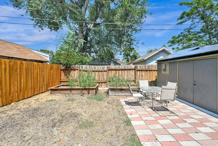 Patio with checkered pavers, raised garden beds, wood privacy fencing, and a storage shed with solar panels