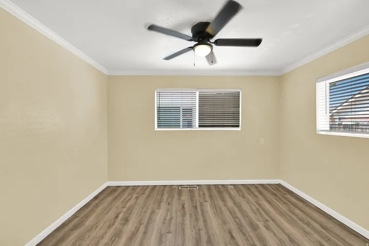 Wood-finish flooring, crown molding, ceiling fan with integrated lighting, and dual windows with blinds