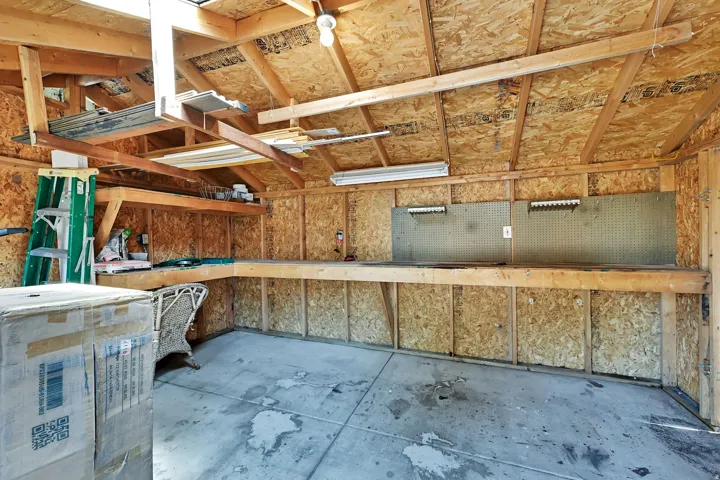 Exposed wood beam ceiling, concrete flooring, built-in shelving, pegboard wall panels, and fluorescent lighting fixtures