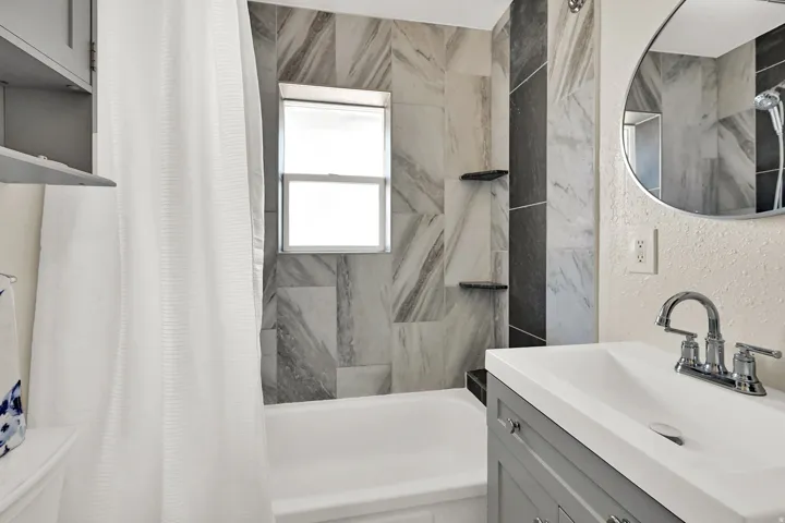 Bathtub with a window, tiled shower surround, recessed shower shelves, and a vanity with an integrated sink and chrome faucet
