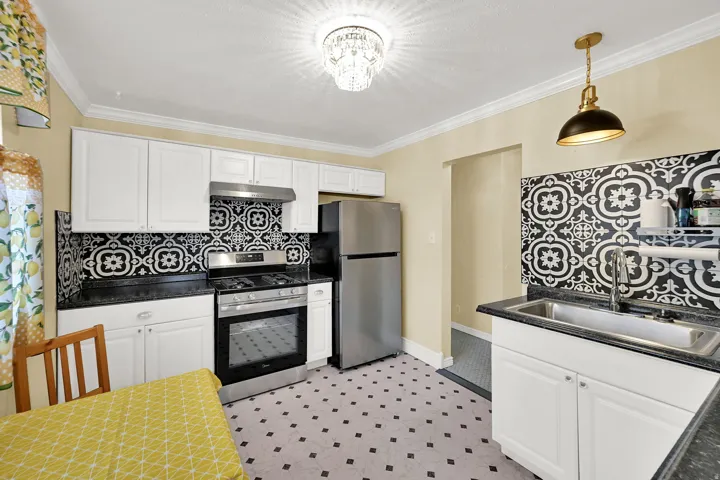 White cabinetry, patterned tile backsplash, stainless steel appliances, black countertops, and patterned floor tiles